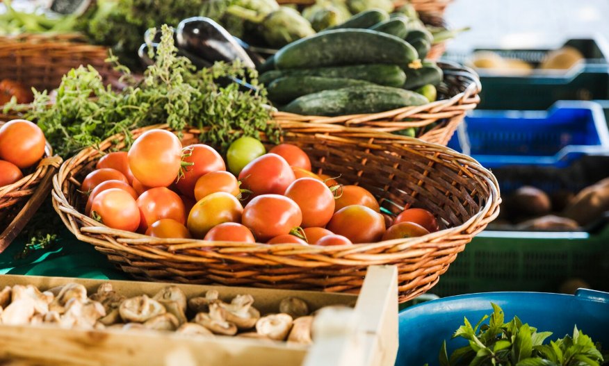 Baskets of fresh tomatoes, cucumbers, herbs, and mushrooms at a market stall