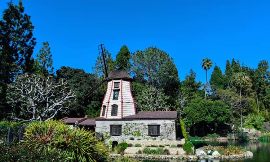A stone windmill house beside a pond surrounded by trees under a blue sky